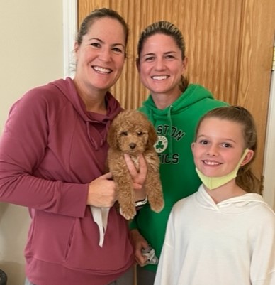 two adult women and a young girl holding a goldendoodle puppy